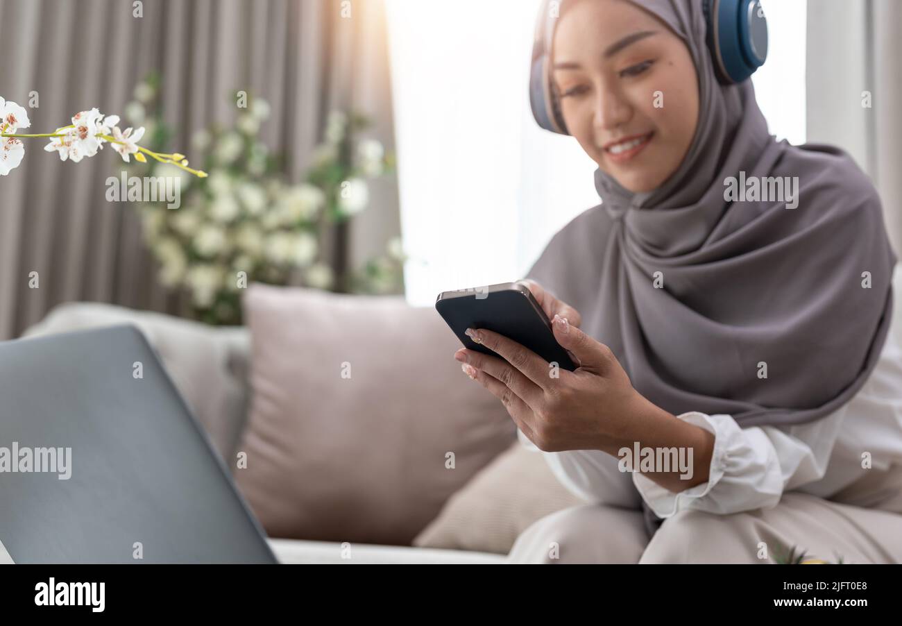 Muslimische Frau, die Mobiltelefon benutzt und im Bürozimmer sitzt. Nahaufnahme Stockfoto