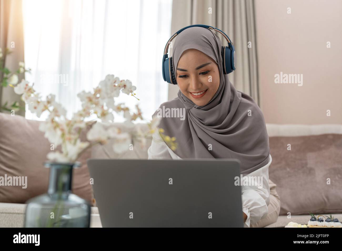 Asiatische muslimische Dame trägt Kopfhörer Webinar ansehen Online-Kurs anhören Kommunizieren Sie per Konferenz Videoanruf in der Nacht Home Office. Remote-Arbeiten von aus Stockfoto