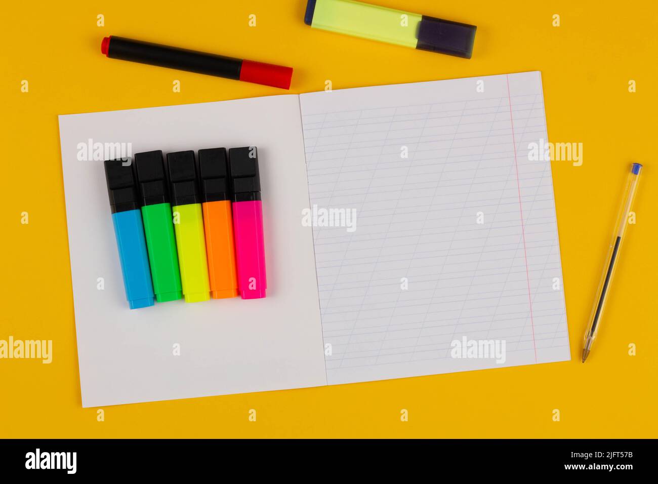 Schulnotizbuch auf gelbem Hintergrund mit Platz für Text, bunten Markern und Stift. Zurück zur Schule. Leeres Blatt Papier mit schrägen Linien in Stockfoto