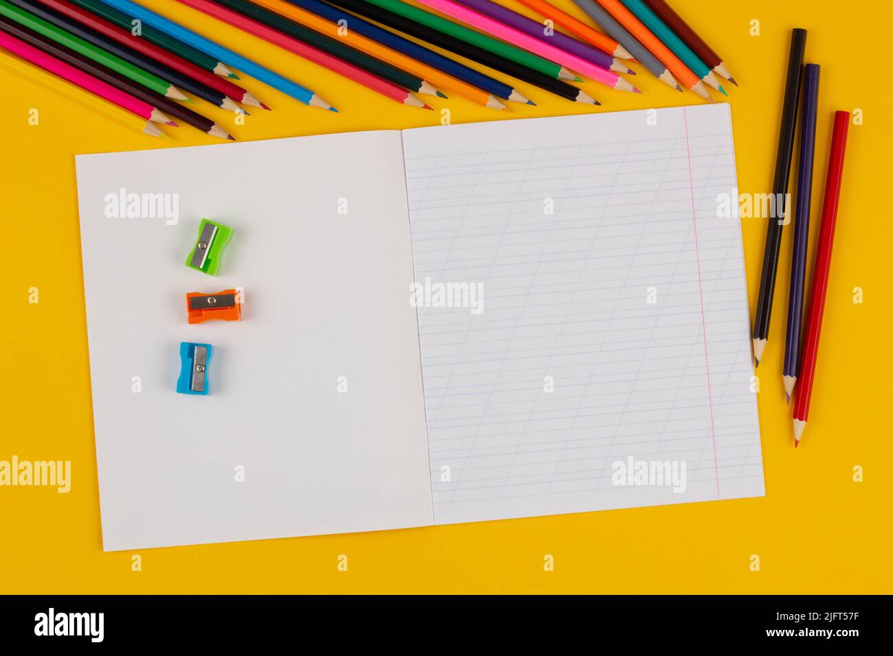 Schulheft auf gelbem Hintergrund mit Text aus dem Textbereich, Buntstiften, Bleistiften und Spitzern. Zurück zur Schule. Leeres Blatt Papier mit schräg Stockfoto