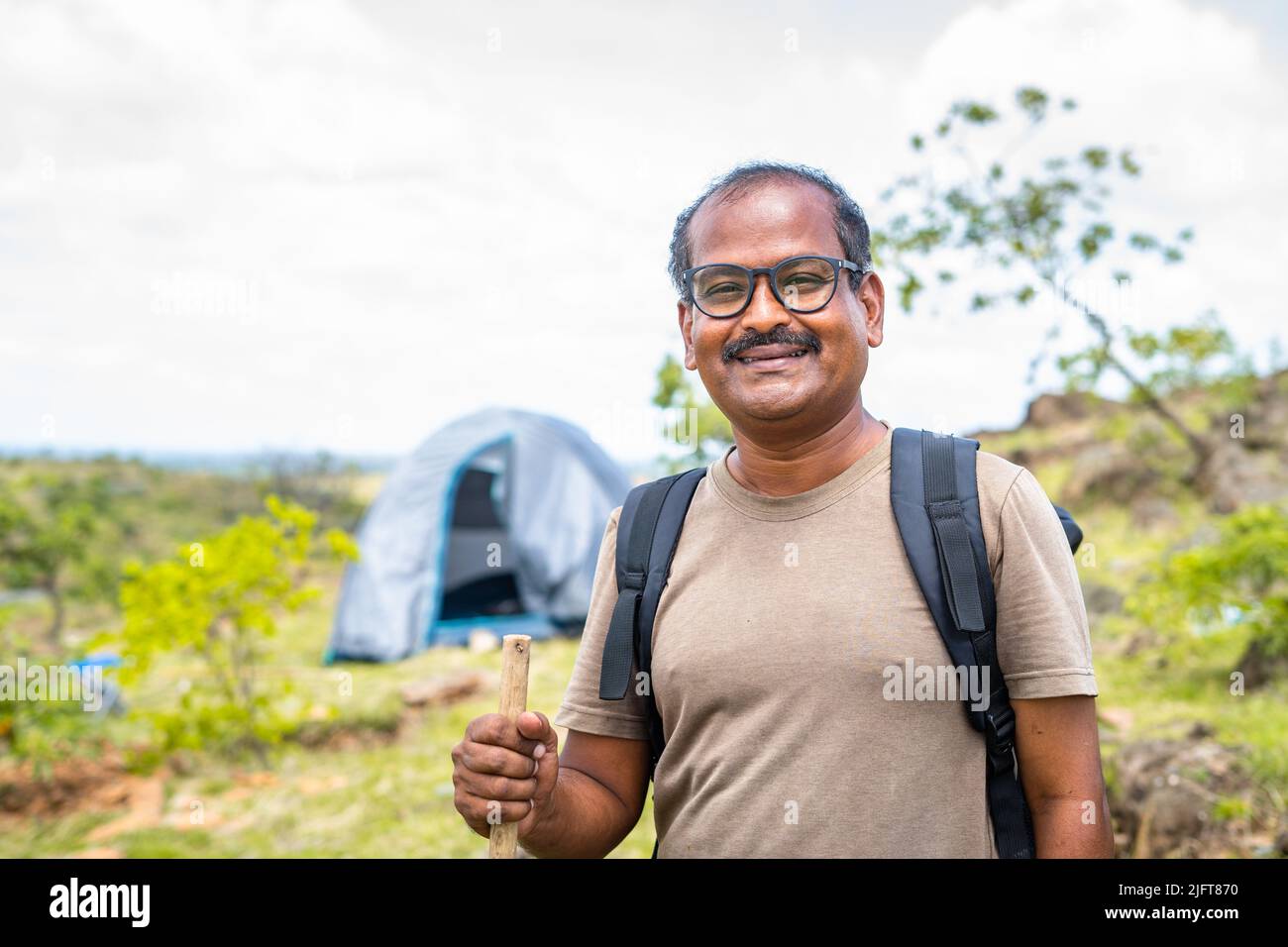 Porträt eines glücklichen lächelnden Reisenden mit Wanderstock vor dem Zelt und Blick auf die Kamera - Konzept von Hobby, Urlaub und Urlaub. Stockfoto