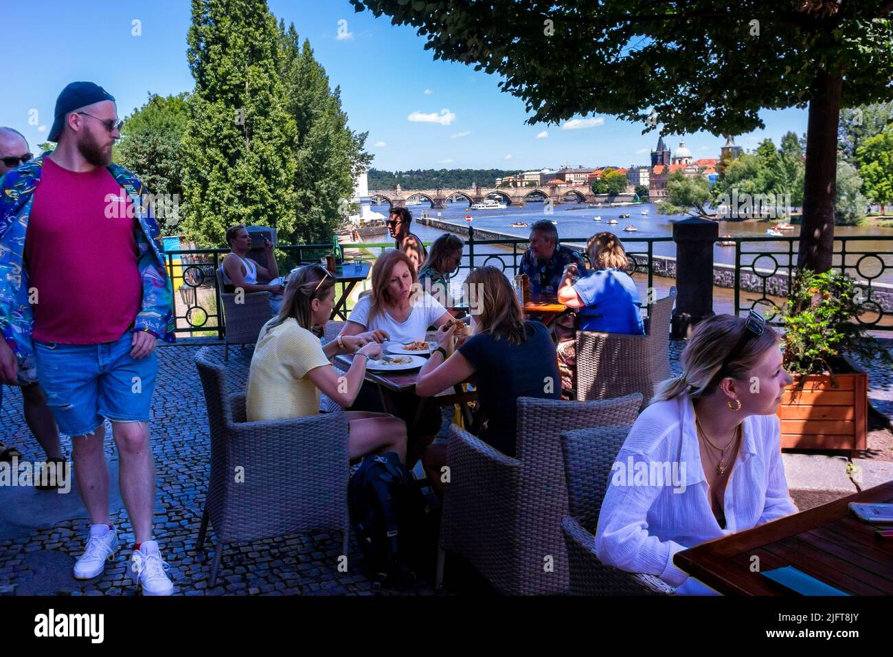 Prag, Tschechische Republik, Menschenmenge beim gemeinsamen Essen auf der Bistro-Restaurant-Terrasse am Fluss Vlava, szenischer Sommer, Bistro-Tisch im Garten Stockfoto