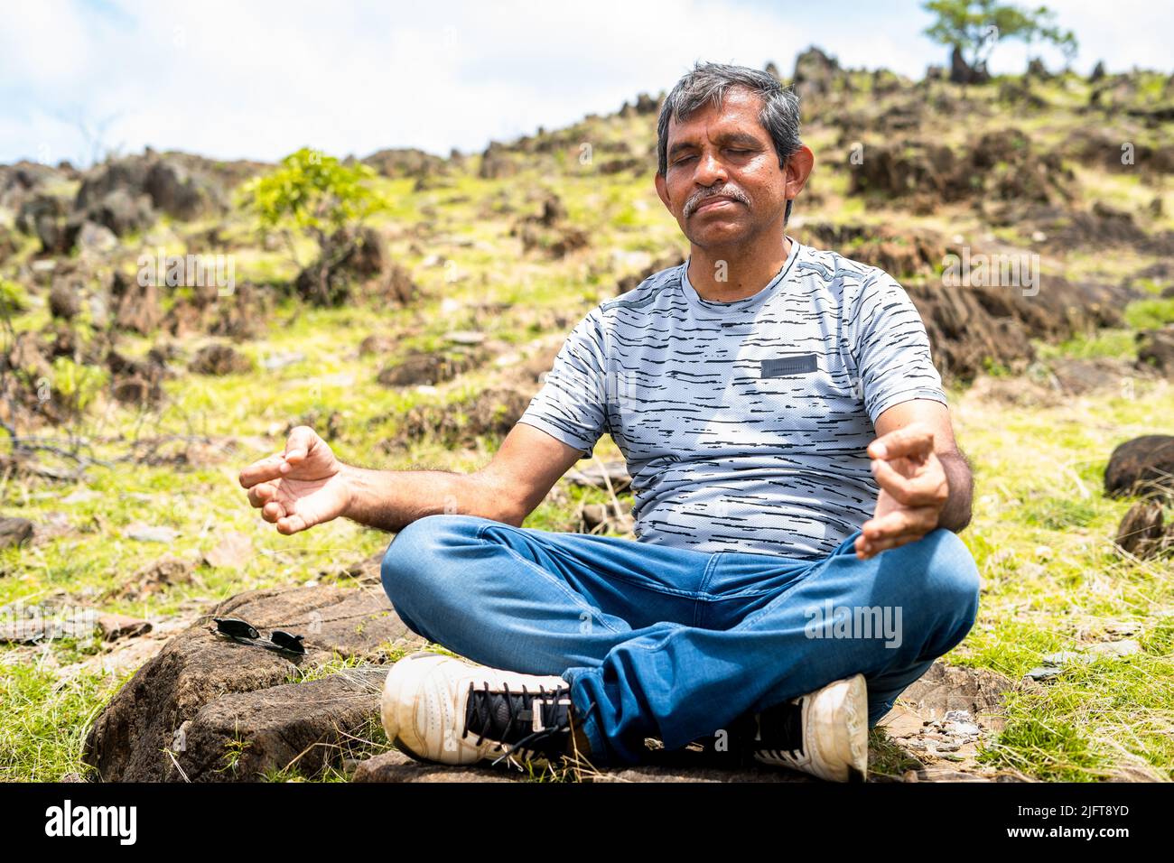 Mann mittleren Alters mit geschlossenen Augen, der während des Monrings Meditation auf dem Hügel macht - ein Gestacheltes auf Achtsamkeit, Selbstversorgung und Ruhe Stockfoto