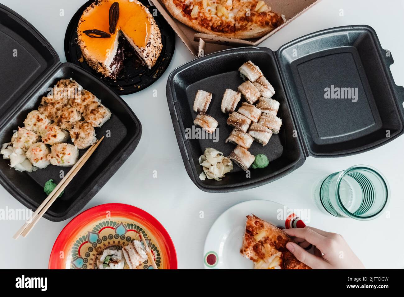 Partytisch mit Essen zum Mitnehmen in Plastikverpackung. Pizza, Sushi-Brötchen und Kuchenfoto für die Speisekarte. Lieferung von Lebensmitteln Stockfoto