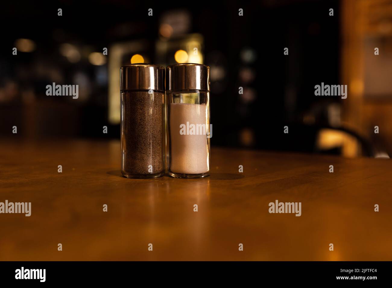 Salz- und Pfefferstreuer stehen auf einem Holztisch in einer dunklen Bar Stockfoto