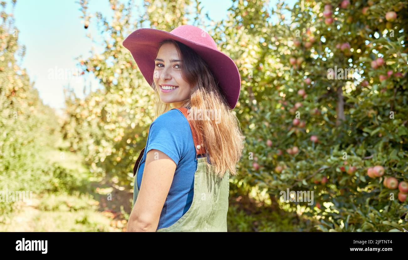 Porträt einer schönen Bauernhofarbeiterin, die während der Erntezeit auf einer Obstfarm steht. Junger glücklicher Bauer an einem sonnigen Tag zwischen Obstbäumen Stockfoto