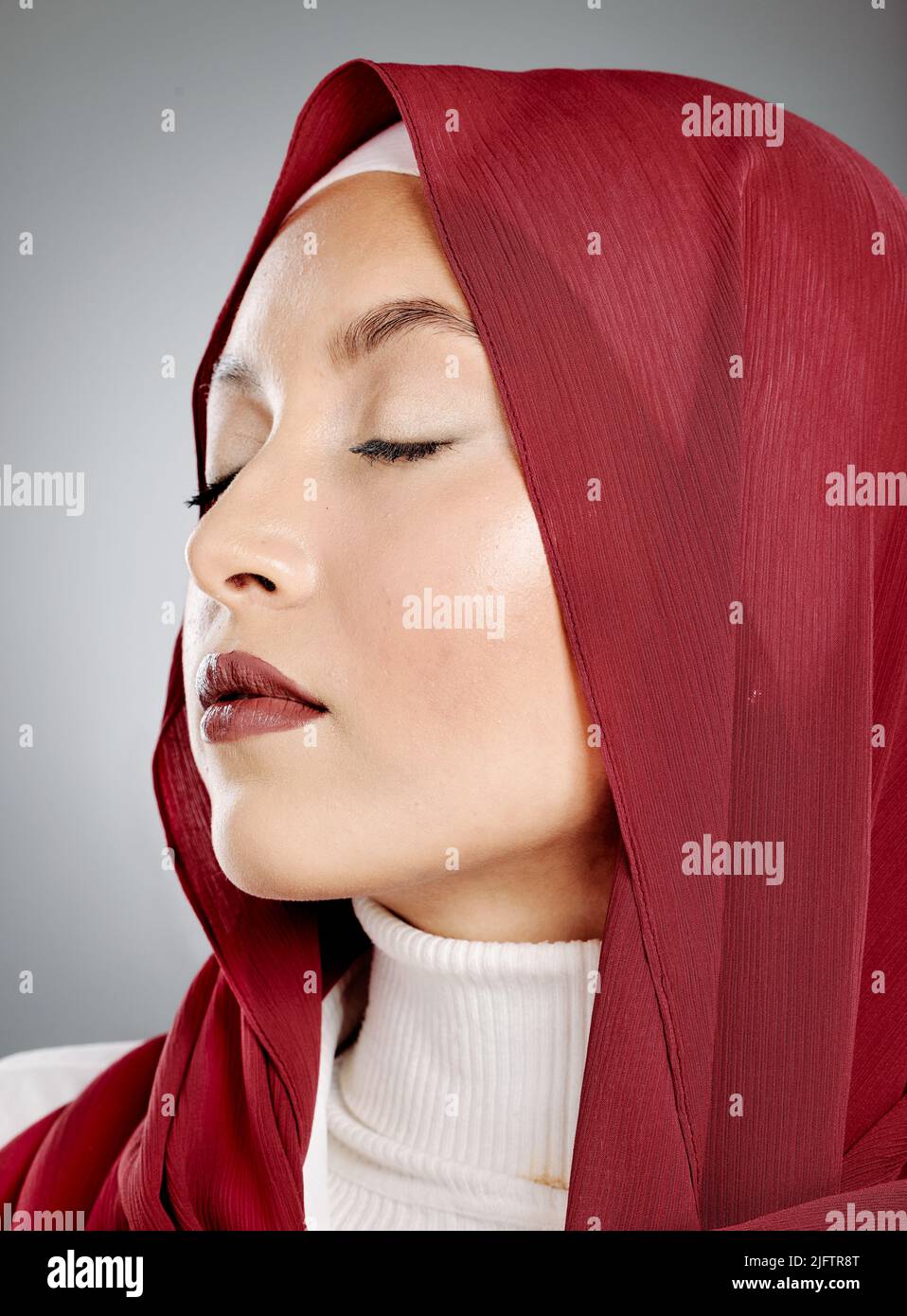 Nahaufnahme einer glühenden schönen muslimischen Frau mit Wimpern-Erweiterungen isoliert vor grauem Hintergrund im Studio. Junge Frau trägt einen roten Hijab oder Stockfoto