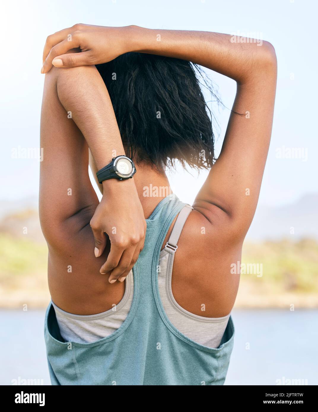 Eine aktive Frau vom Rücken, die Arme und Trizeps streckt, indem sie den Ellbogen zur Wirbelsäule zieht, während sie im Freien trainiert. Weibliche Athletin beim Aufwärmen Stockfoto