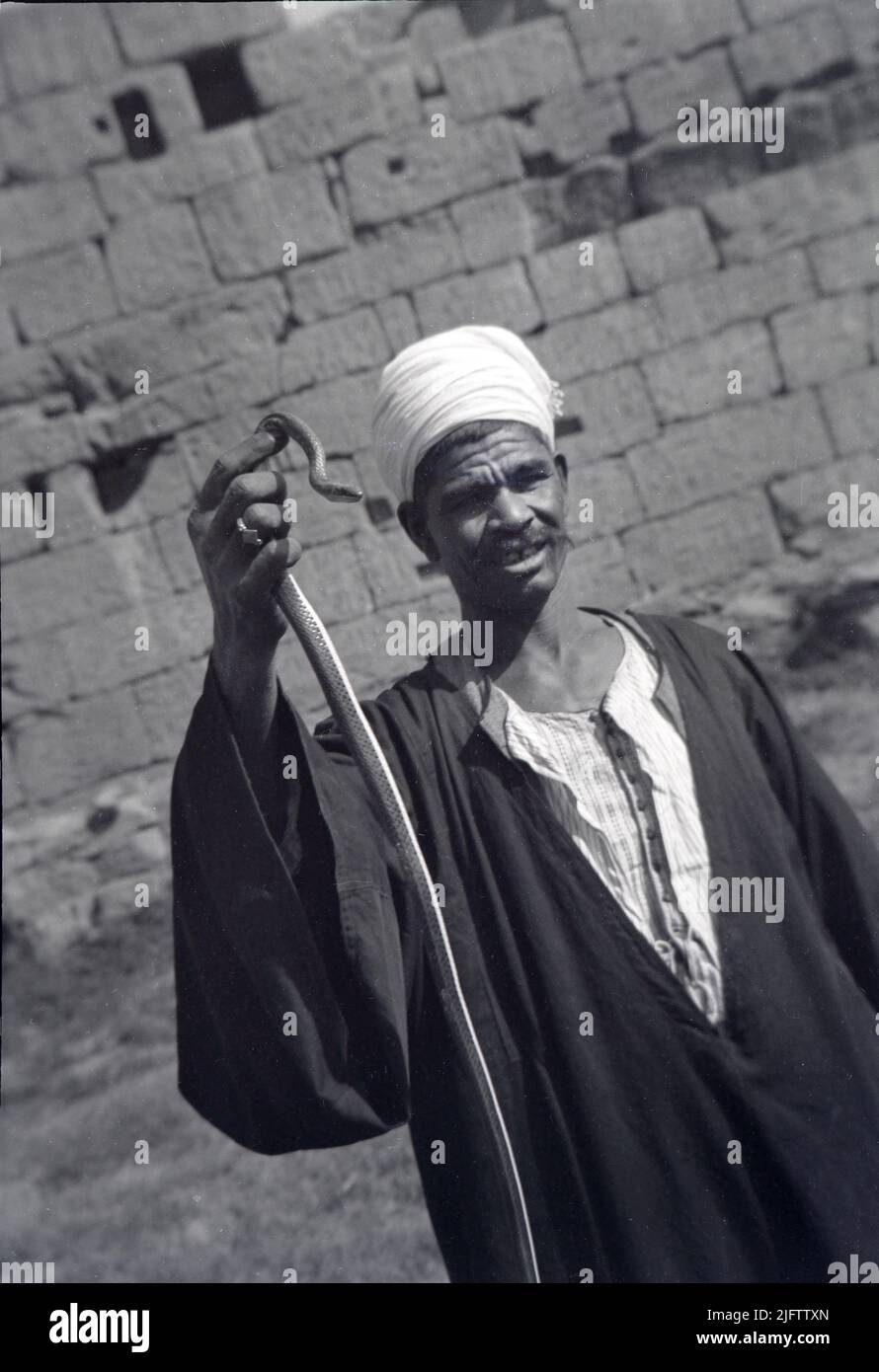 1940s Vintage-Foto eines ägyptischen Mannes, der eine Schlange am Tempel Karnak in Luxor hält Stockfoto