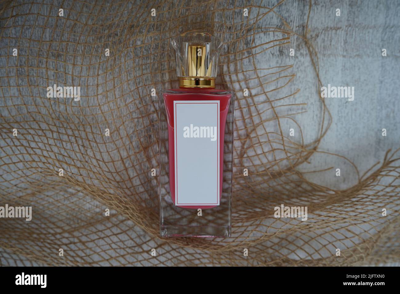 Rote Parfüm-Flasche mit weißem leeren Rechteck und Goldkappe, auf einem weißen Holzhintergrund und Sackleinen Parfüm Mockup. Und 3D Rendering Stockfoto
