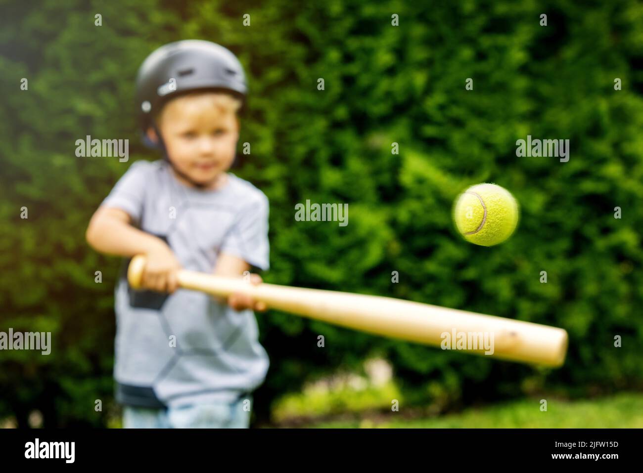 Kleiner Junge trifft Tennisball mit Baseballschläger im Hinterhof zu Hause Stockfoto