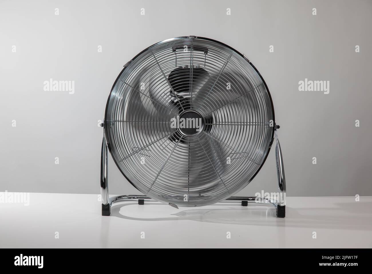 Silberner Metallbodenventilator auf dem weißen Boden zu Hause oder im Geschäft mit grauer Wand. Stockfoto