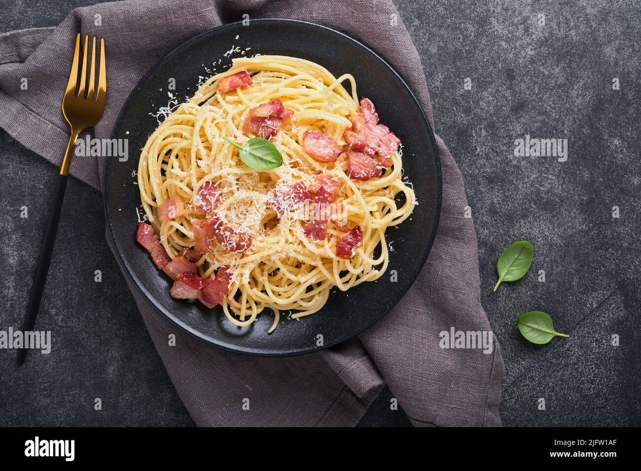 Carbonara Pasta. Spaghetti mit Pancetta, Ei, Parmesankäse und Sahnesauce auf altem dunkelschwarzen Betontisch-Hintergrund. Traditionelle italienische Küche Stockfoto