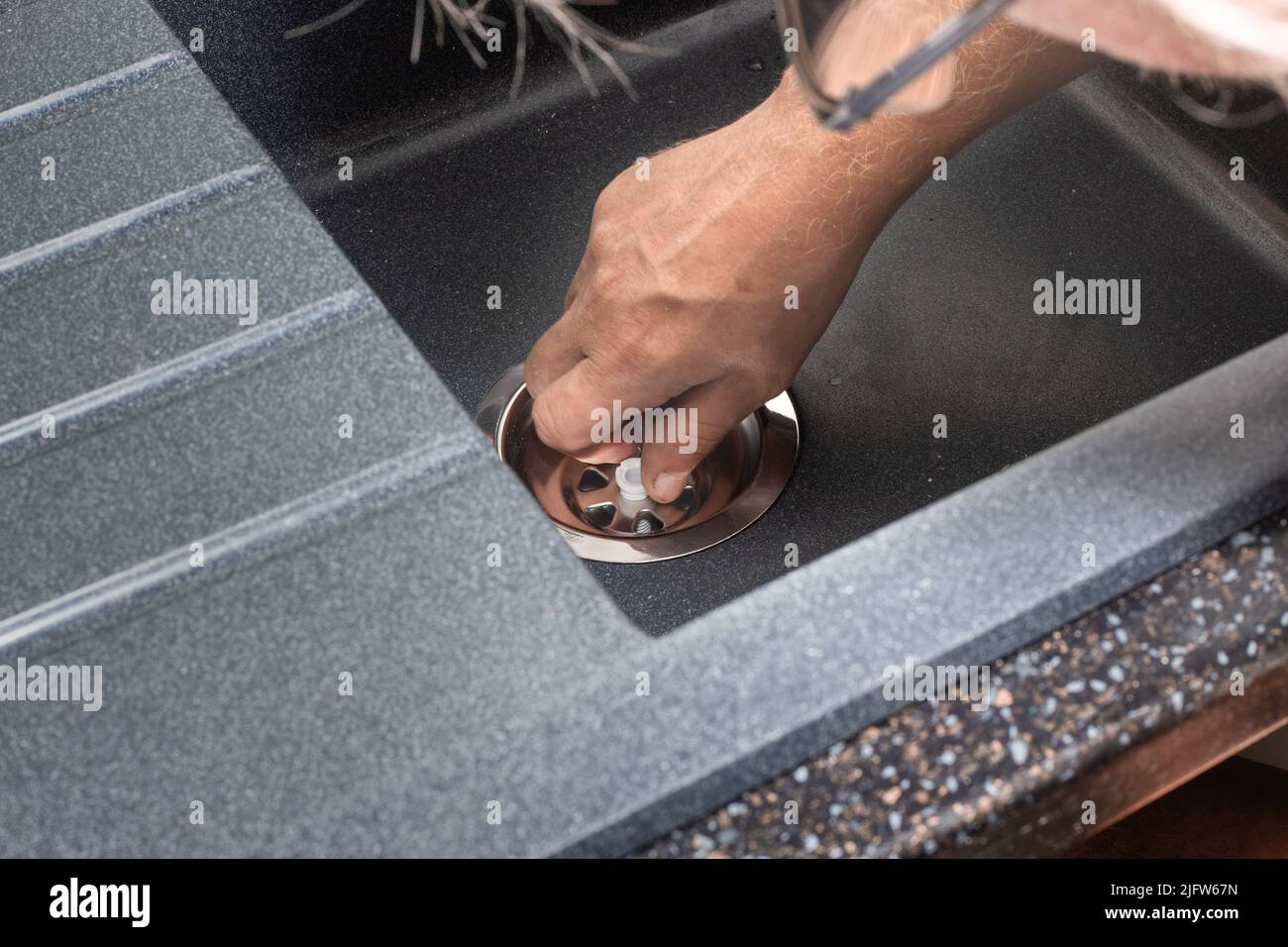 Ein Mann installiert ein neues Spülbecken und montiert einen Siphon in das Loch. Hausreparaturen. Stockfoto