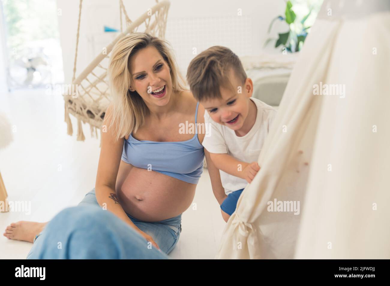 Fröhliche, schwanger Mutter und ihr Sohn sitzen auf dem Boden und haben Spaß. Hochwertige Fotos Stockfoto