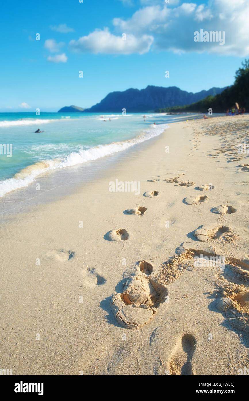 Ein leerer Strand, entspannende Sommerseeseite für einen ruhigen Urlaub mit klarem blauen Himmel Kopieplatz und Fußabdrücke in der Sandtapete. Waves Washing Stockfoto