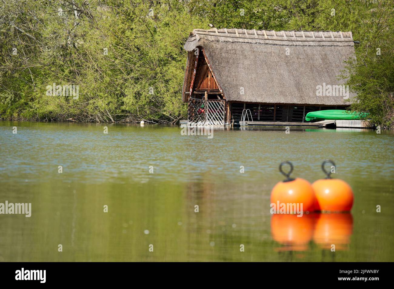 Stuttgart, 22. April 2022: Bootshaus auf dem See. Bauen auf dem Wasser mit grünen Booten. Orangefarbene Bojen im Vordergrund. Deutschland, Stuttgart Stockfoto