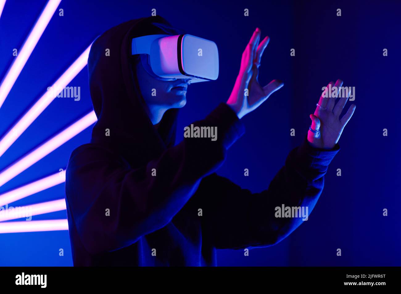 Futuristische Aufnahme einer jungen Frau, die ein VR-Headset in 3 Dimensionen mit Neonlichtschranken trägt, mit Kopierraum Stockfoto