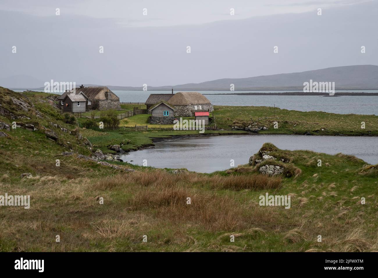 Zwei alte reetgedeckte Cottages und Nebenhäuser an einer Bucht in der Nähe des Berneray Harbour, in The Sound of Harris, Berneray Isle, Outer Hebrides, Schottland. Stockfoto