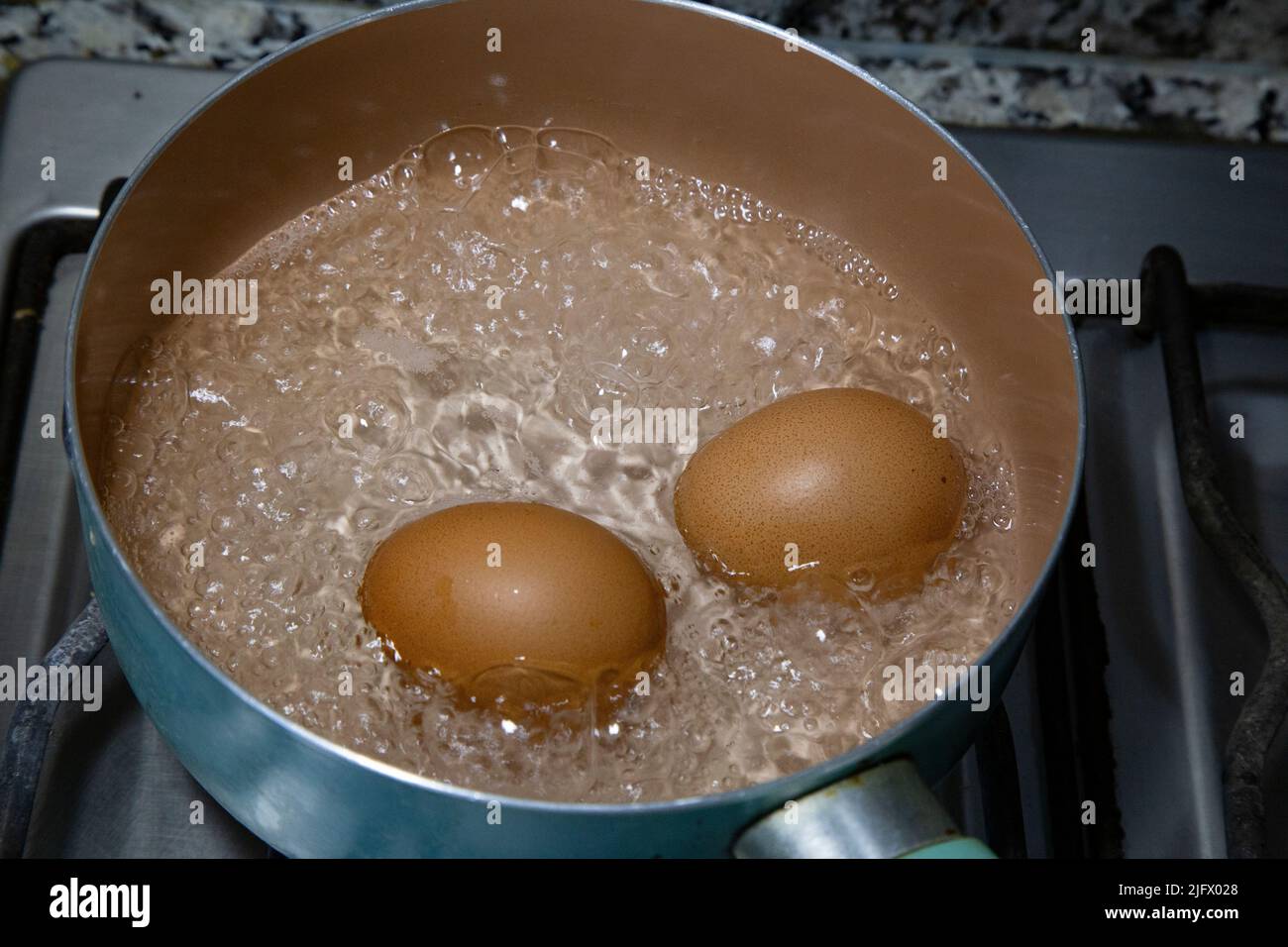 Hühnereier, die in Wasser in einem hellblauen Topf auf dem Herd kochten. Stockfoto