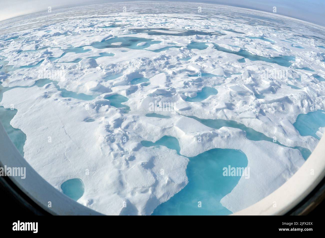 Fischaugen-Blick durch ein rundes Fenster. ARKTISCHER OZEAN - Eine mehrjährige Eisscholle rutscht auf der Steuerbordseite des Küstenwache-Schneiters Healy hinunter, während das Schiff in Richtung Norden in noch dickeres Eis fährt. „Man kann erkennen, dass es sich um eine mehrjährige Eisscholle durch die hellblauen Schmelzteiche handelt, die sich auf der Scholle gebildet haben“, sagte Pablo Clemente-Col, leitender Wissenschaftler am US-amerikanischen National Ice Center. Arctic Ocean, August (2009) Quelle: P.Kelley, USCG Stockfoto