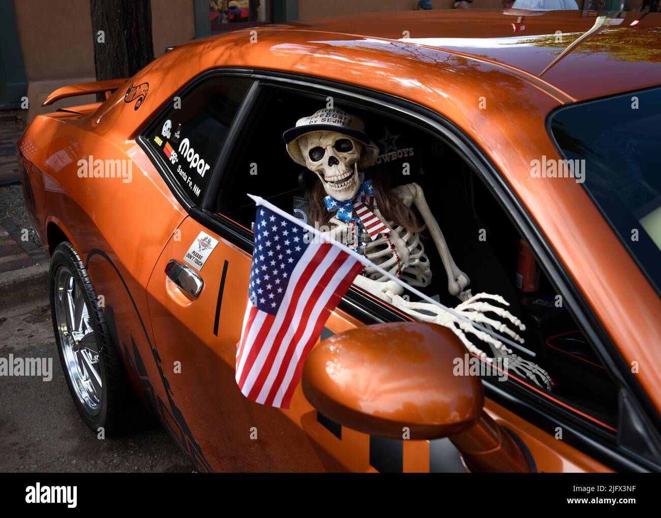 Ein neuheitliches Kunststoff-Skelett hält eine amerikanische Flagge in einem Dodge Challenger aus dem Jahr 2011, der auf einer Automobilausstellung am 4. Juli in Santa Fe, New Mexico, ausgestellt wird. Stockfoto