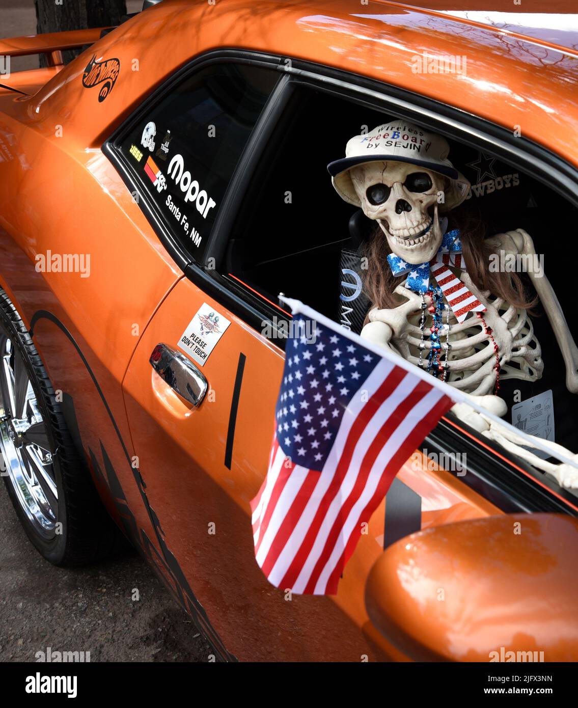 Ein neuheitliches Kunststoff-Skelett hält eine amerikanische Flagge in einem Dodge Challenger aus dem Jahr 2011, der auf einer Automobilausstellung am 4. Juli in Santa Fe, New Mexico, ausgestellt wird. Stockfoto