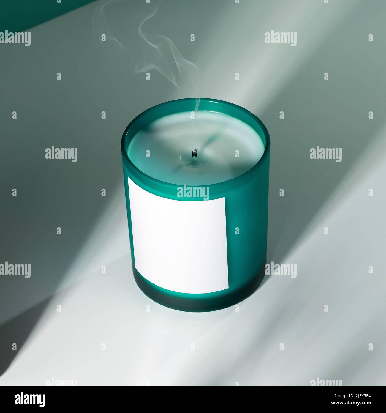 Duftkerze aus Sojawachs in einem Aquamarin-Glas mit Schatten. Ein kreatives Bild einer aromatischen Kerze mit einem Rauch aus dem Docht.das Konzept der Gemütlichkeit Stockfoto