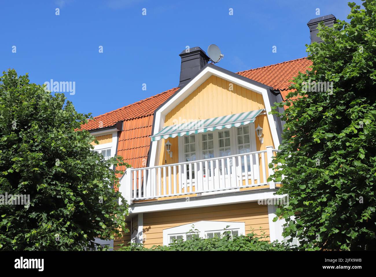 Freistehendes zweistöckiges gelbes Holzfamilienhaus hinter dem Gartengrün. Stockfoto