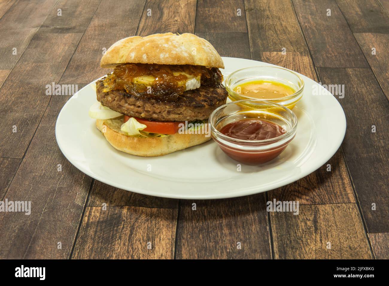 Burger mit Rinderfilet, Ziegenkäse, karamellisierten Zwiebeln, Tomaten und Salat sowie Tomaten- und Senfsoße Stockfoto