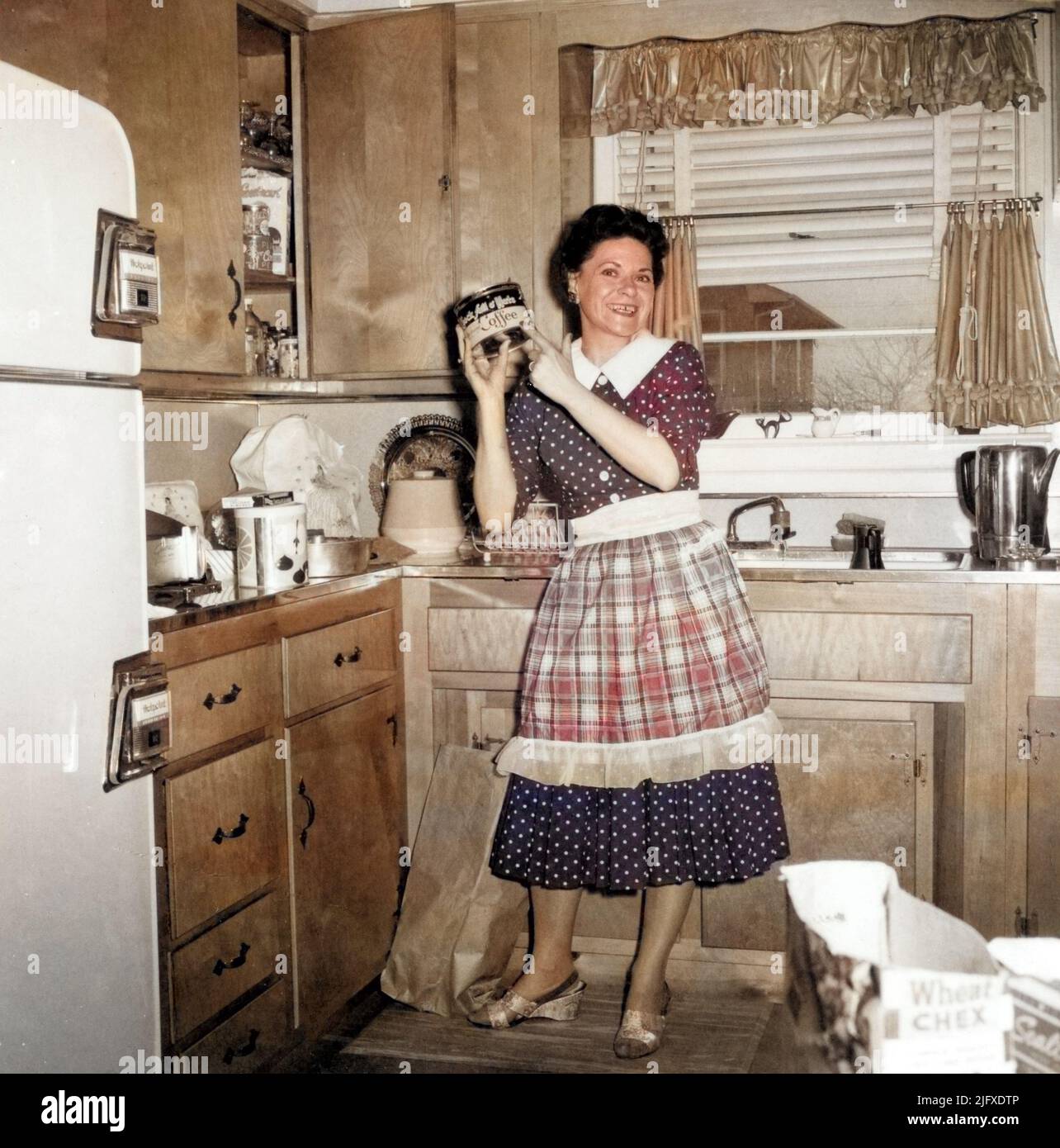 Junge Hausfrau in der Vorstadt in ihrer Küche, die eine Dose Chock Full o' Nuts Kaffee hochhält, um 1950s, USA. Stockfoto