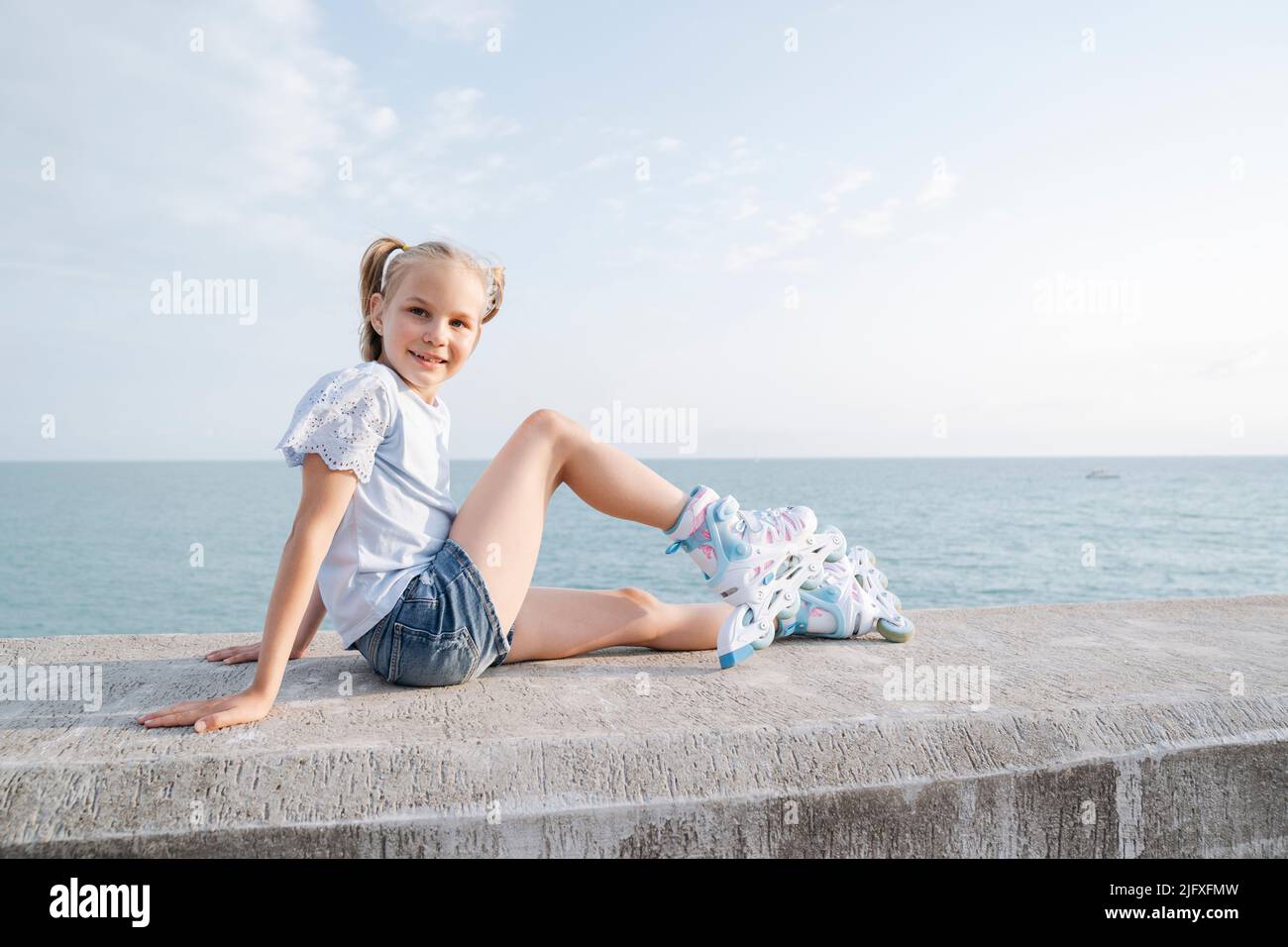 Ein Mädchen in Rollschullaufbahn sitzt am Meer. Stockfoto