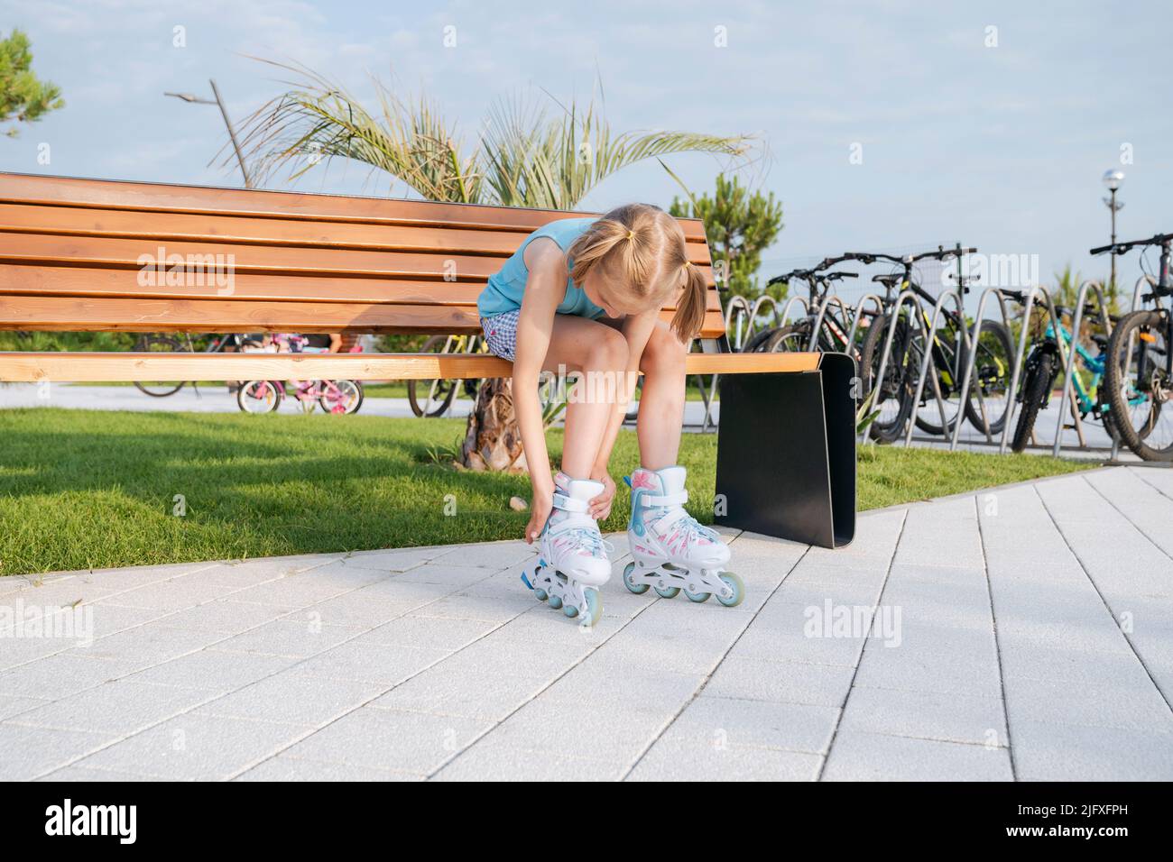 Ein Mädchen in Rollschullaufenwagen befestigt in einem Park auf einer Bank ein Rollschloss. Stockfoto