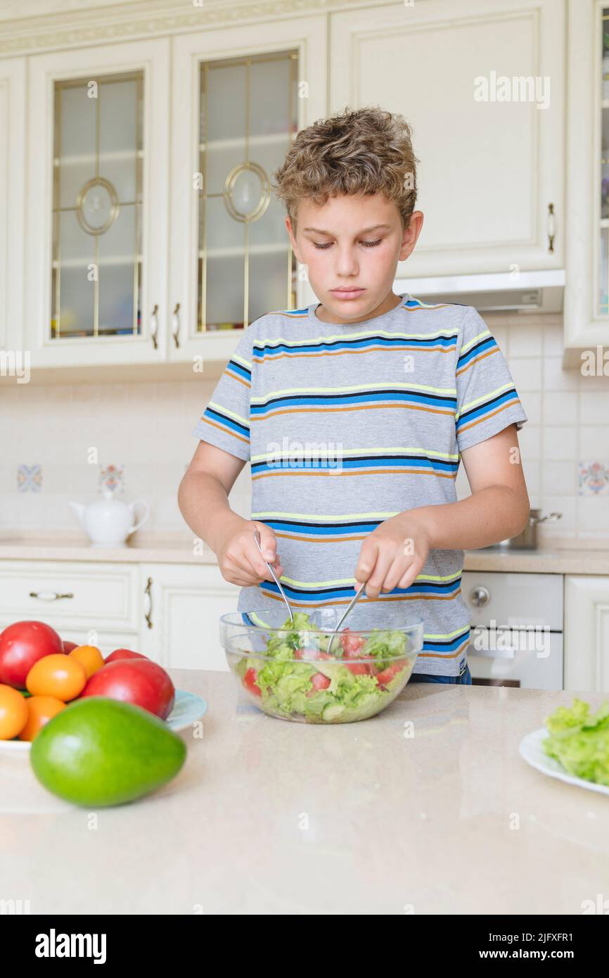 Ein 11-jähriger Junge kocht selbst einen Salat aus Gemüse. Stockfoto
