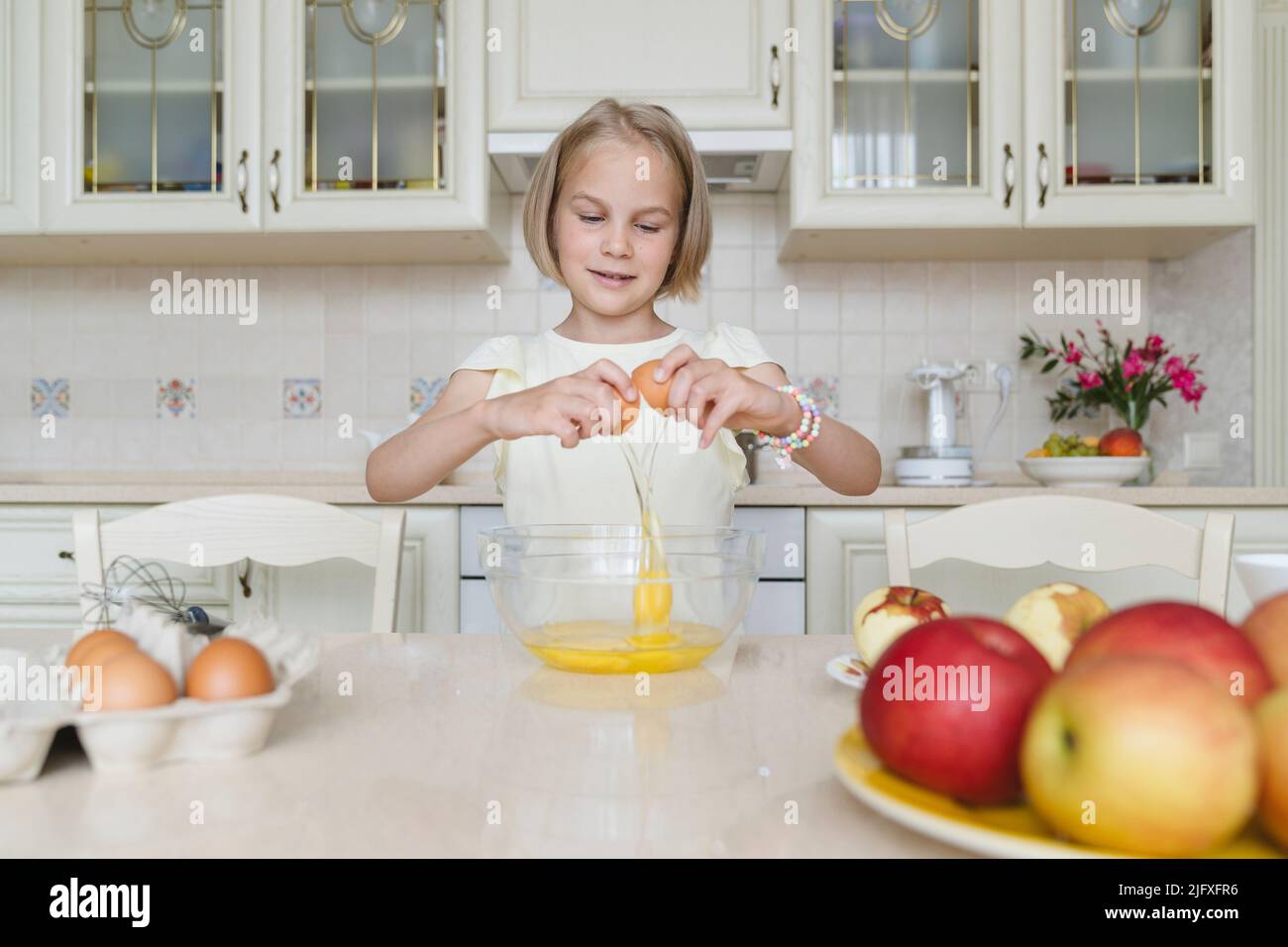 Ein 8-jähriges Mädchen zu Hause in der Küche bricht ein Ei, kocht einen Kuchen. Stockfoto