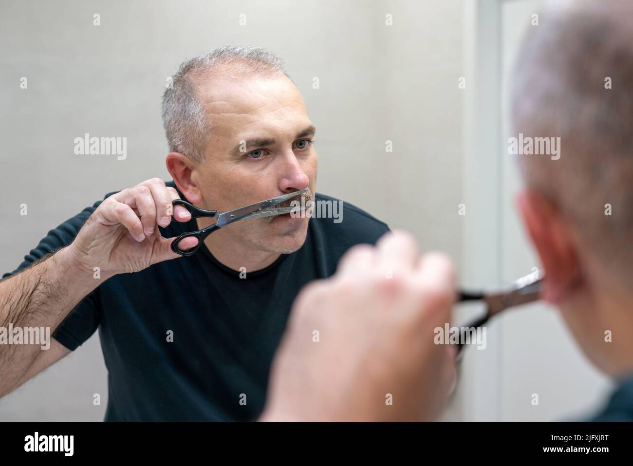Gutaussehender Mann mittleren Alters, der mit einer Schere seinen Schnurrbart Schnitt Stockfoto