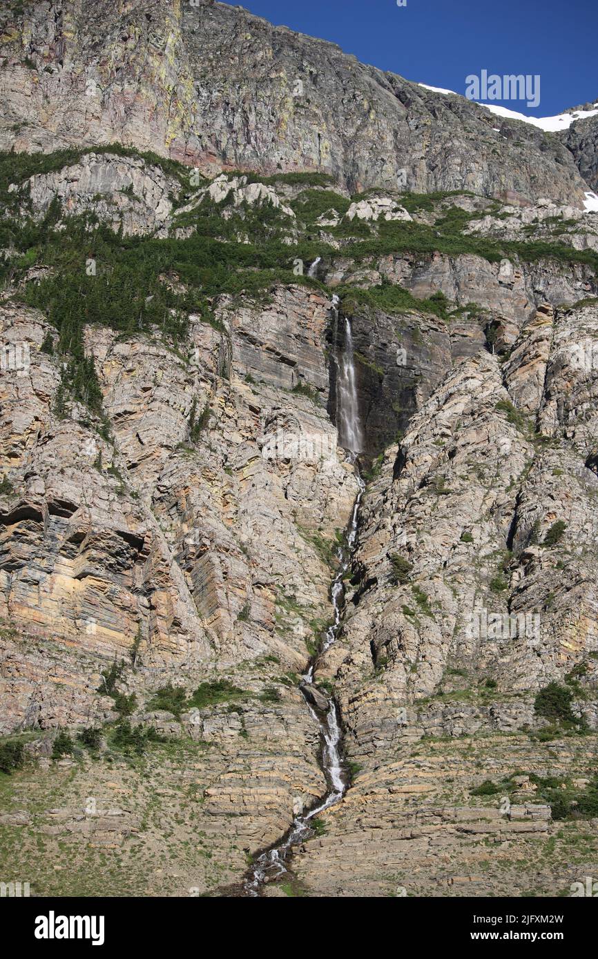 Makelloser Wasserfall, farbenfrohe Felsklippen, grüne Pinien, Piegan & Siyeh Pass Trailhead, geht zur Sun Road, Glacier National Park, MT, USA Stockfoto