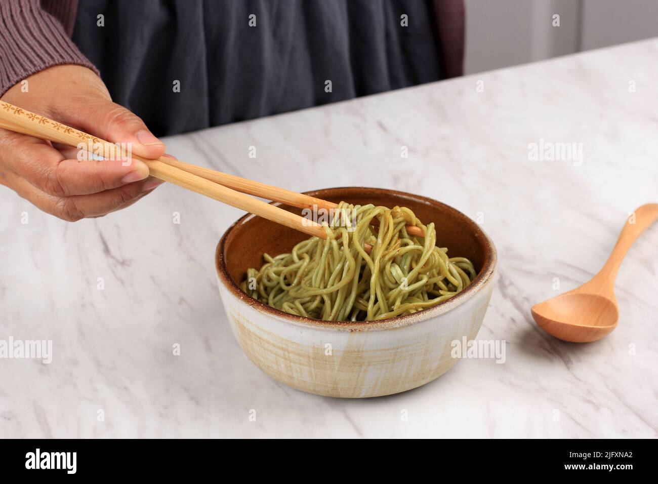 Asiatische weibliche Hand Mix Green Instant gebratenen Noodle mit Gewürz mit einem Paar Chopstick Stockfoto