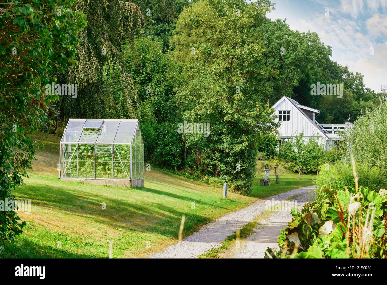 Altes Barnhouse. Ein Eingang zu einem schönen Gewächshaus mit einem üppigen Garten auf dem Rasen. Eine Landschaft Landschaft Blick auf ein weißes Holzhaus, hoch Stockfoto