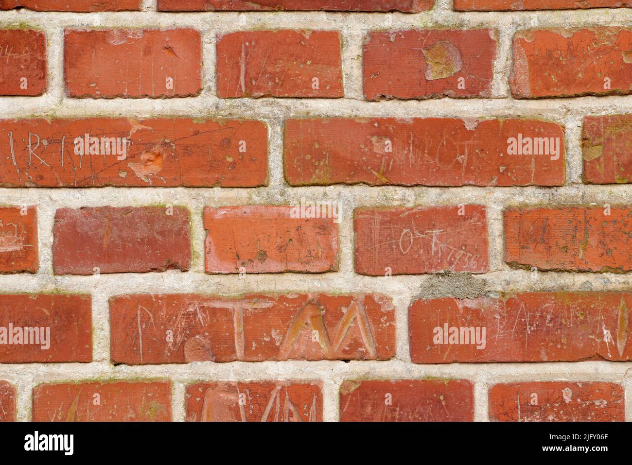 Geschnitzte Schrift auf einer soliden roten Ziegelwand eines Hauses oder Hauses. Nahaufnahme von grober Textur und Detailhintergrund mit Copyspace auf Mauerwerk. Modern Stockfoto