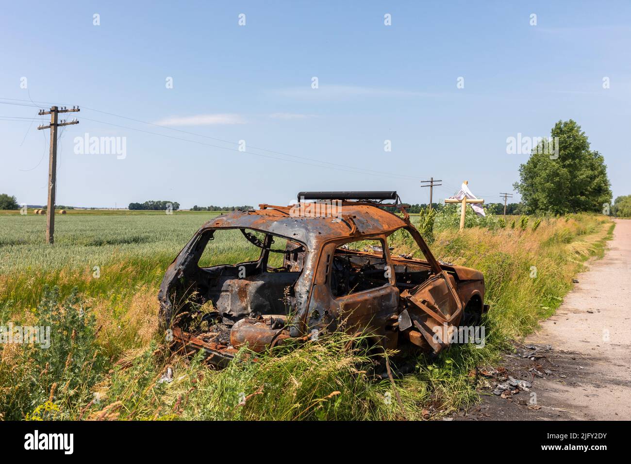 Tschernihiw, Ukraine. 19.. Juni 2022. Ein ausgebranntes Auto am Straßenrand vor dem Hintergrund eines Weizenfeldes und eines schweren Kreuzes. Landschaften der Ukraine nach dem Einmarsch russischer Faschisten. (Bild: © Mykhaylo Palinchak/SOPA Images via ZUMA Press Wire) Stockfoto