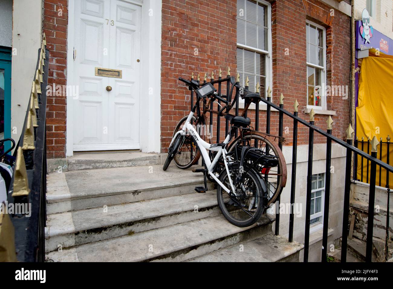 Elektrofahrrad und ein konventionelles Fahrrad werden zusammen und an Geländern befestigt, Weymouth Dorset, England Stockfoto
