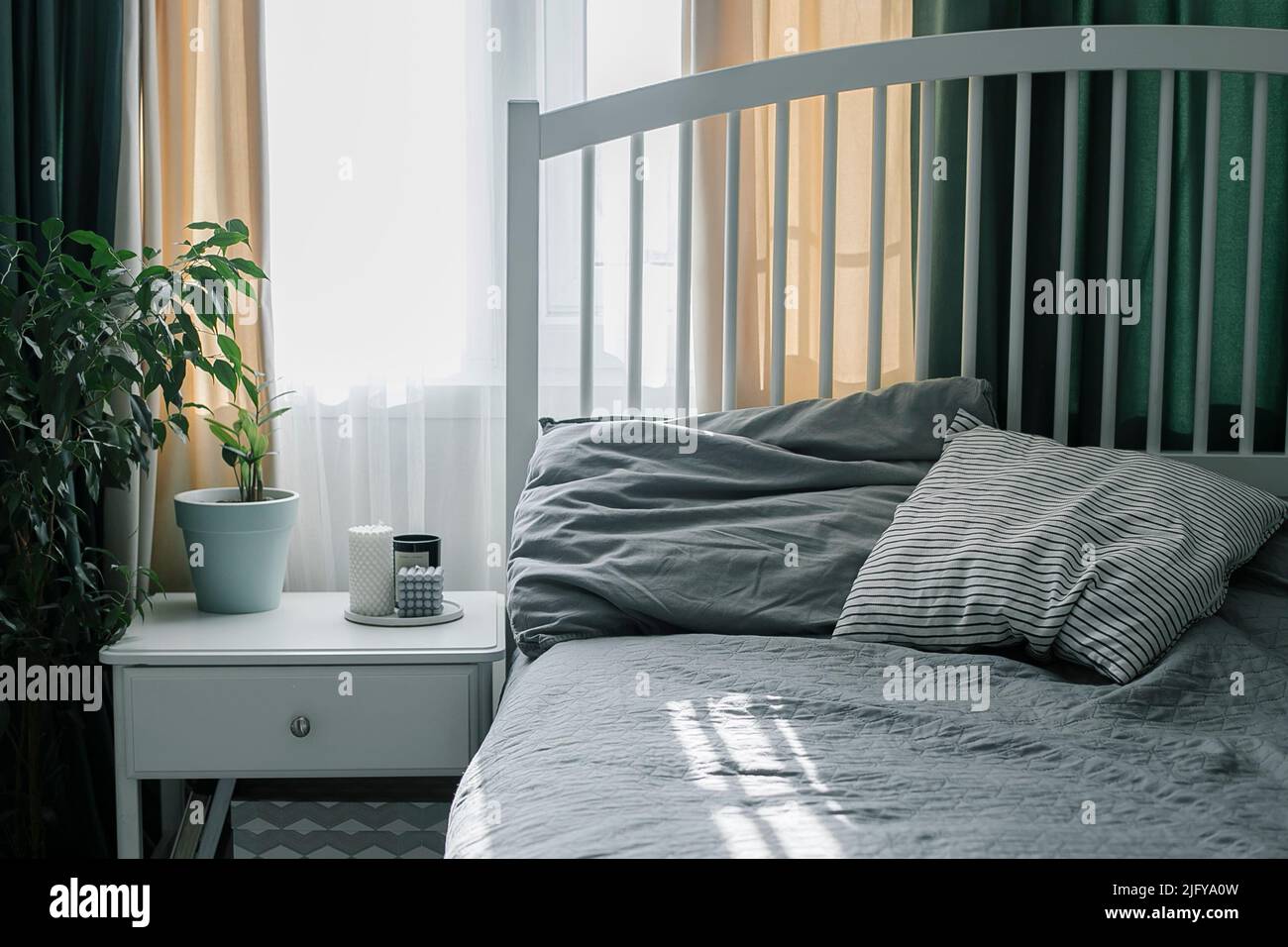 Schlafzimmer mit heller Innenausstattung. Moderne Kerze, Hauspflanze auf Nachttisch neben dem Bett. Lifestyle zu Hause. Stockfoto