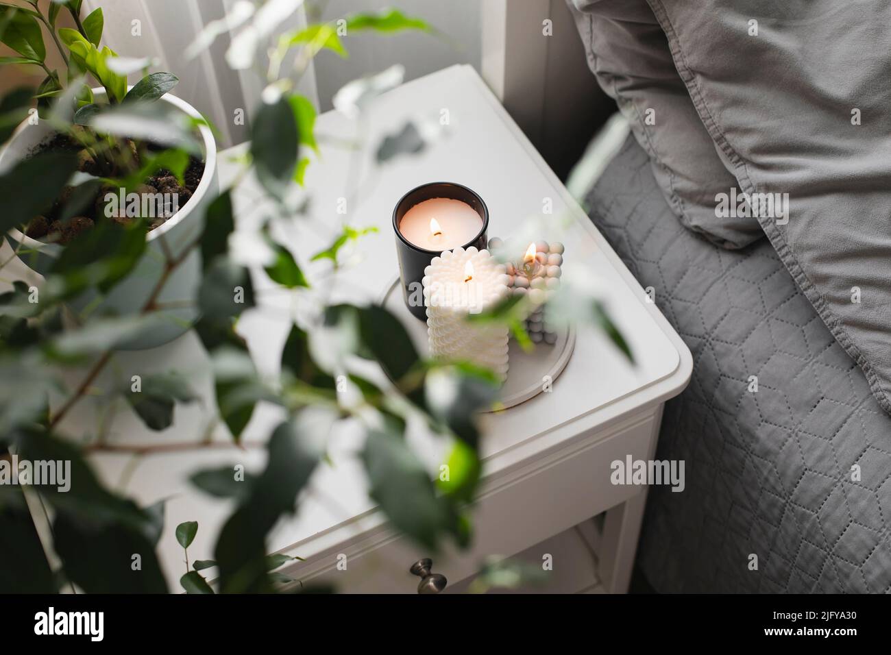 Moderne brennende Kerze auf dem Nachttisch neben dem Bett. Raumduft-Dekor-Konzept. Wellness. Stockfoto