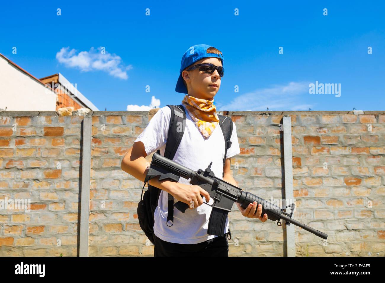 Junger Kaukasusmann mit Brille, die sein automatisches Gewehr M4A1 trägt. Waffengewalt, Schusskonzept. Stockfoto