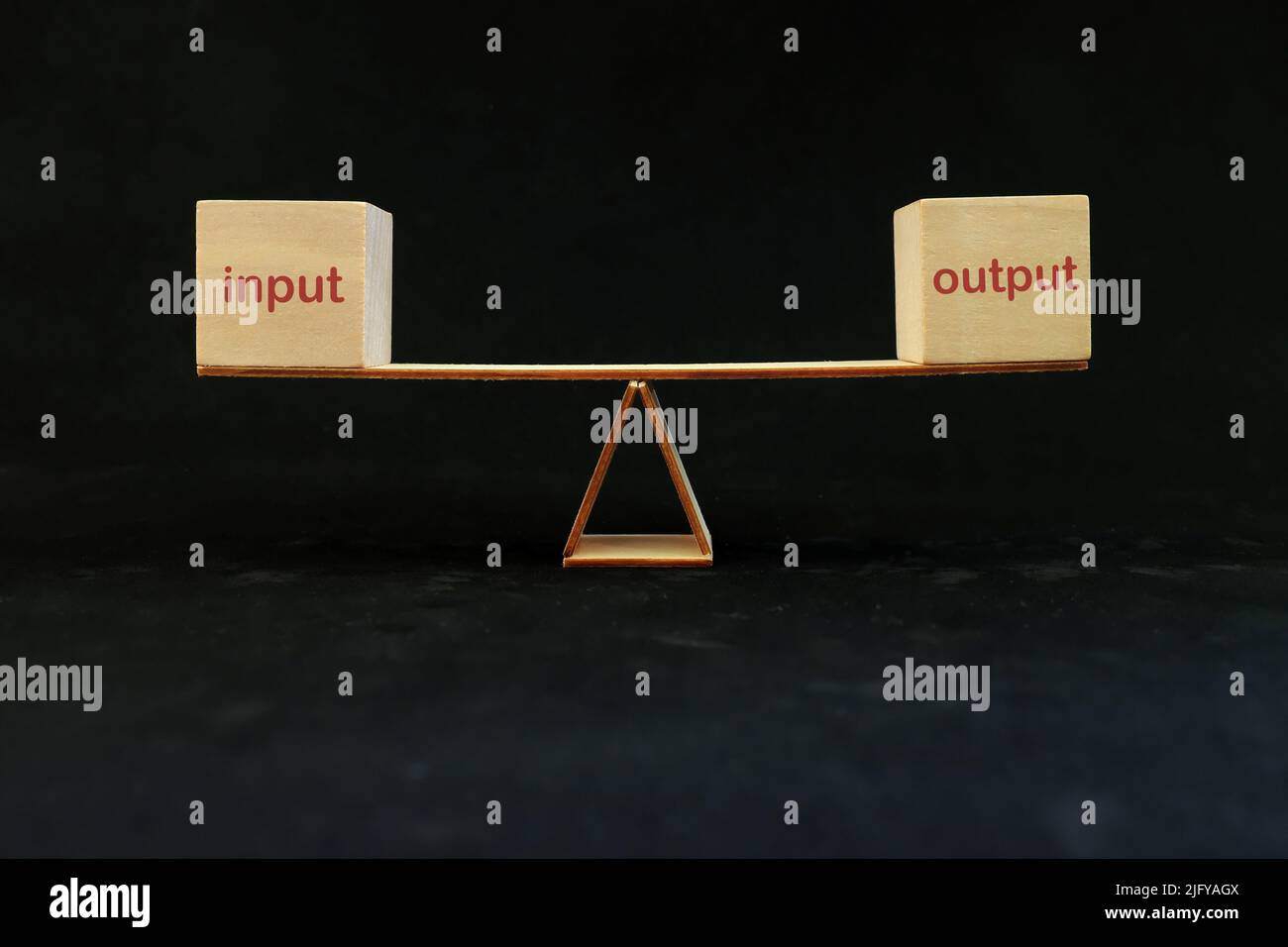 Input entspricht Output-Balance und Prozesseffizienz- und Produktivitätskonzept. Wippe auf dunkelschwarzem Hintergrund. Stockfoto