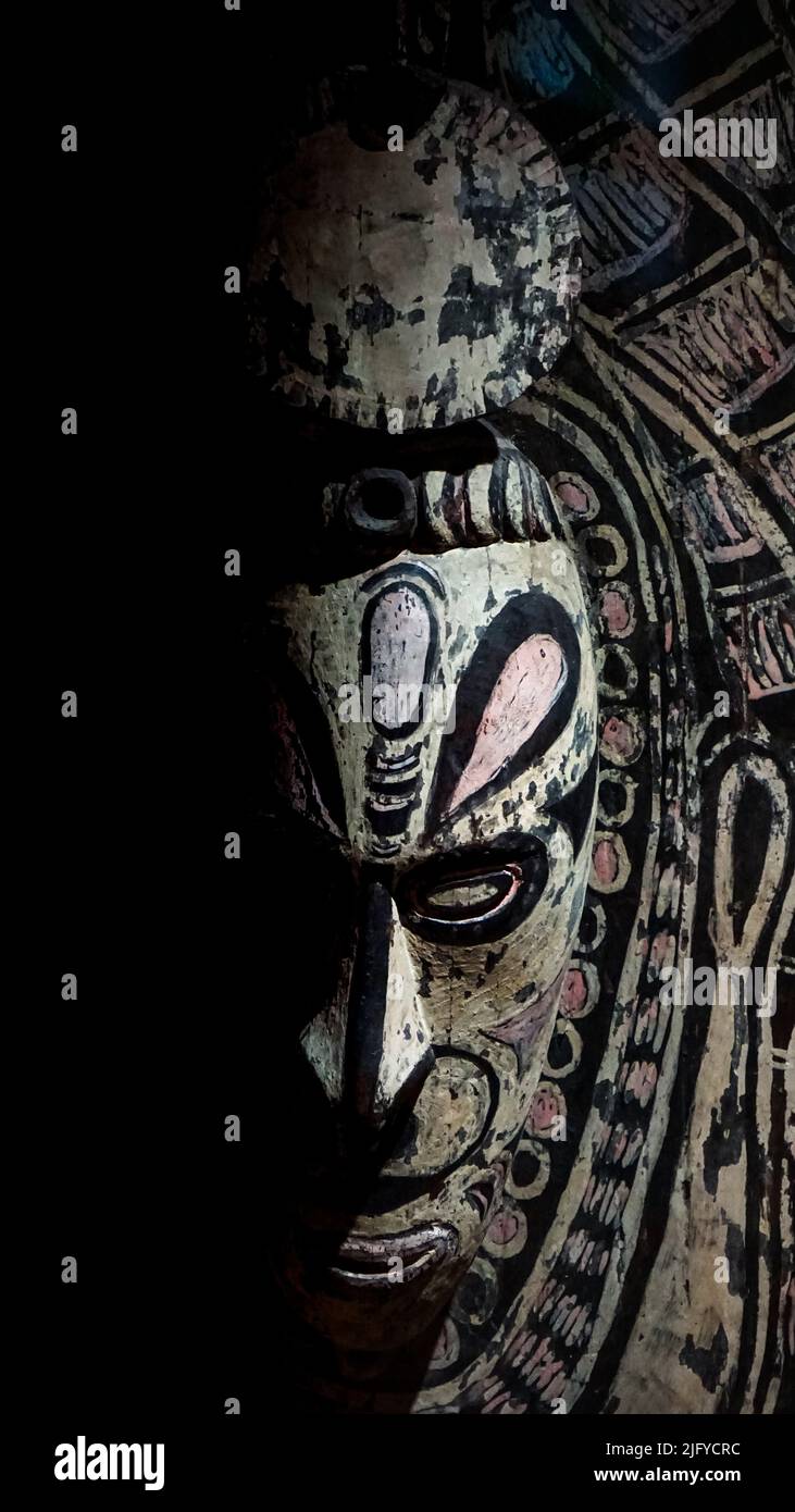 Eine afrikanische Holzmaske, wunderschön geschnitzt und auf einem dramatischen schwarzen Hintergrund bemalt. Stockfoto