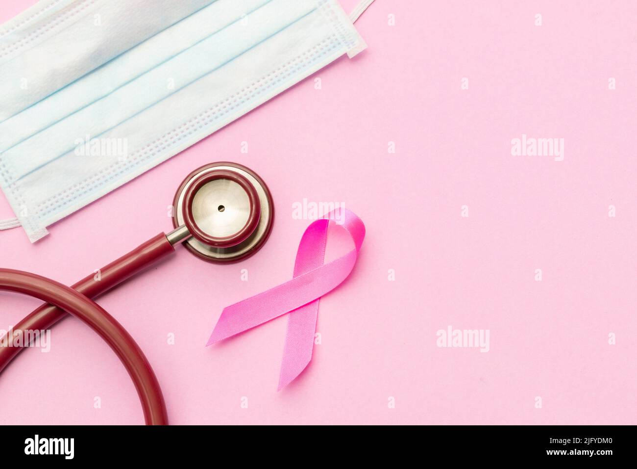 Brustkrebskonzept : Draufsicht rosa Band, rotes Stethoskop und Schutzmaske Symbol der Brustkrebskampagne auf rosa Hintergrund Stockfoto