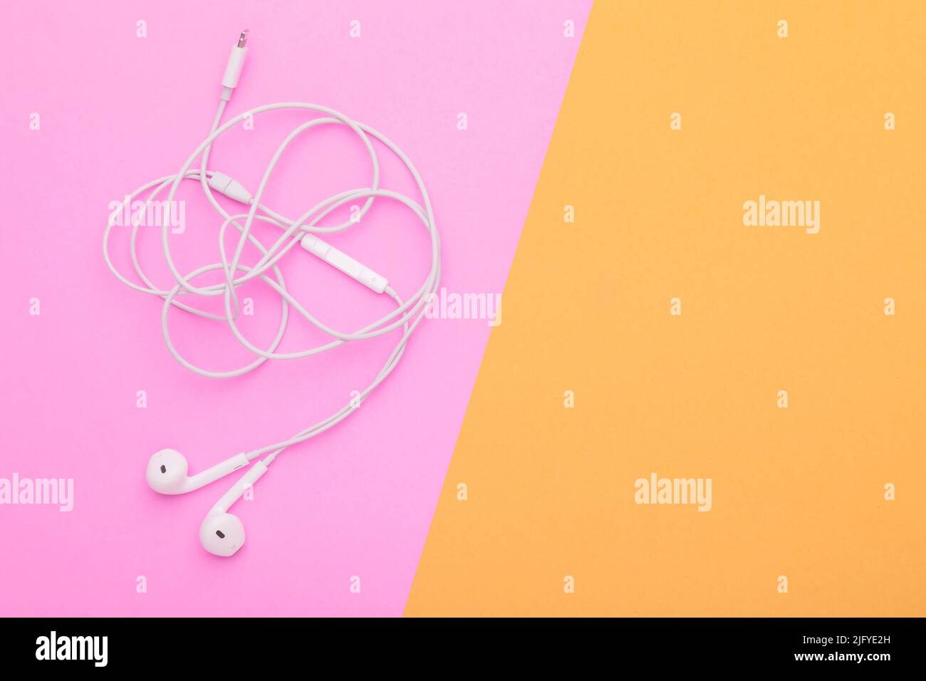 Weißer Ohrhörer mit wirrlichem Gewirr auf rosa Hintergrund. Platz für Text oder Design kopieren Stockfoto