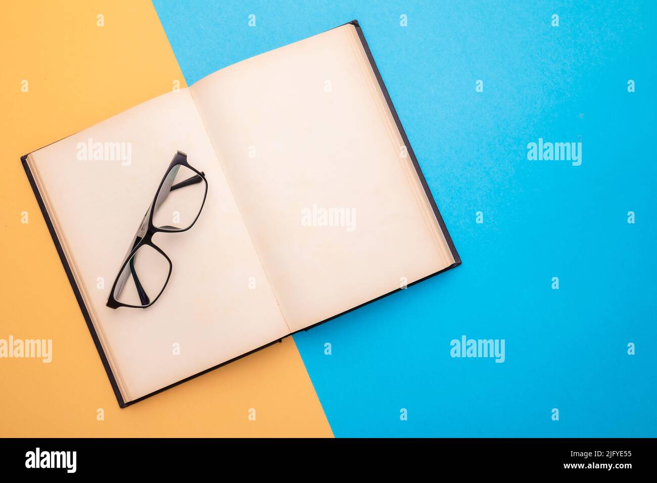 Draufsicht neue Brillen und Buch auf gelbem und blauem Hintergrund. Platz für Text oder Design kopieren Stockfoto